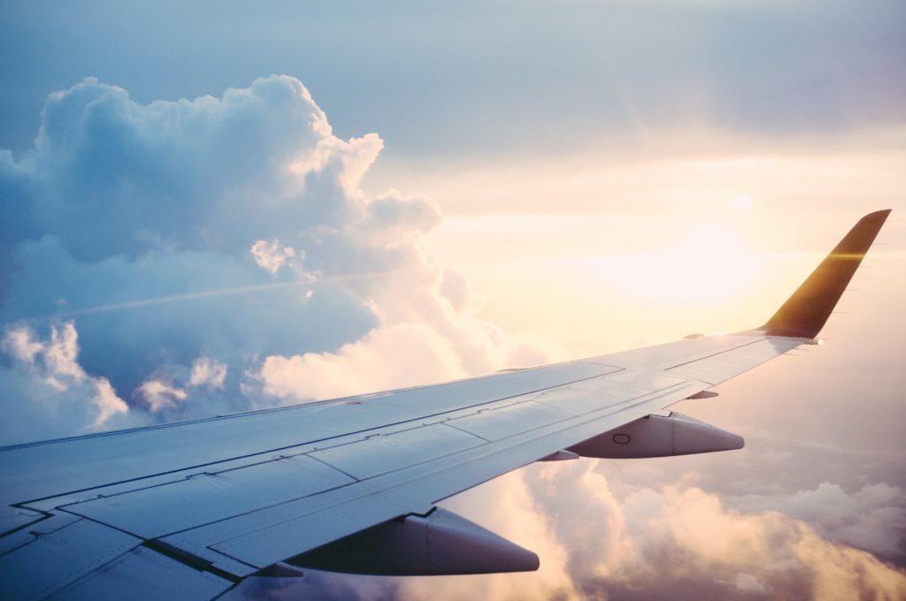 Picture of the wing of a plane in flight with clouds and a sunblaze