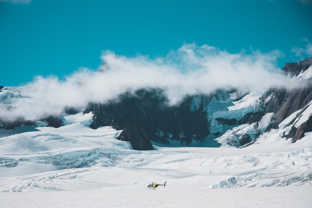 A helicopter landed on the franz josef glacier surrounded by ice, snow, and mountains