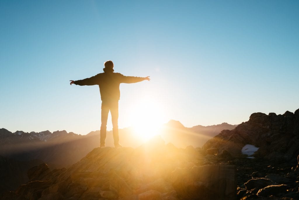 View from the top of Mount Cook with silhouette of a man standing with his arms open welcoming the sun