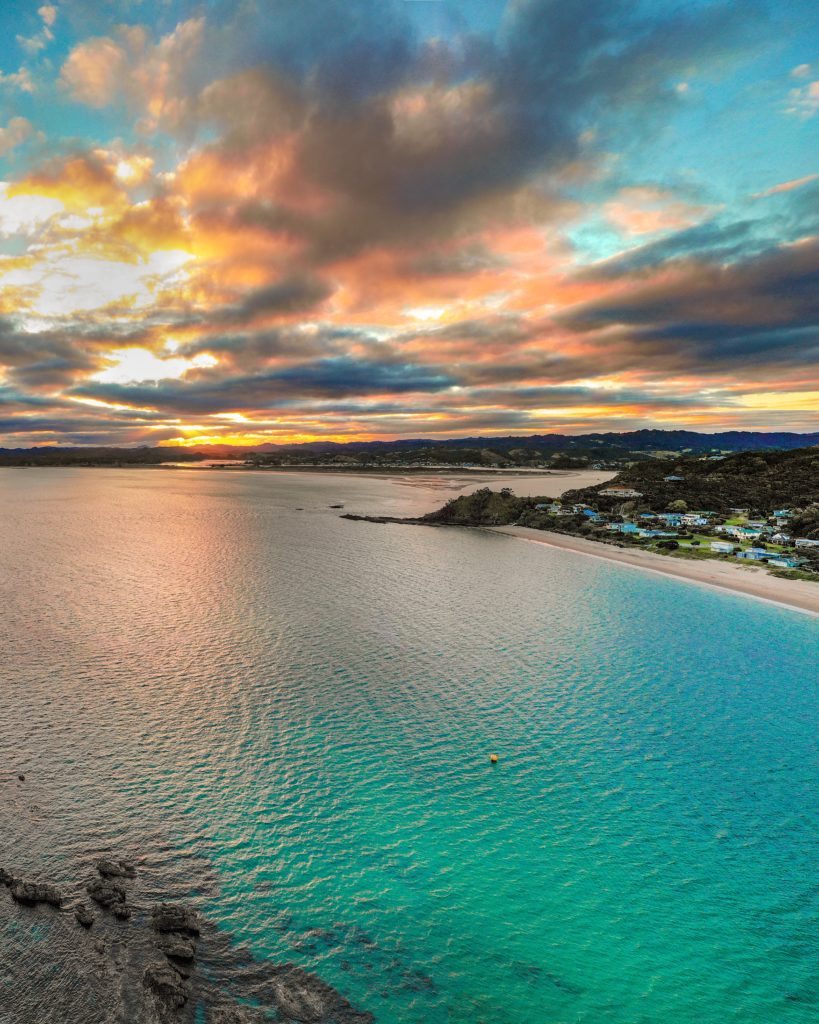 Looking out over bright blue sea at sunset with a snippet of the beach