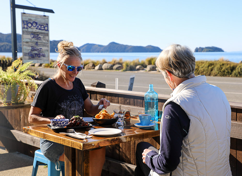 Diners sitting outside Hooked on Marahau restaurant with sea and mountains in background