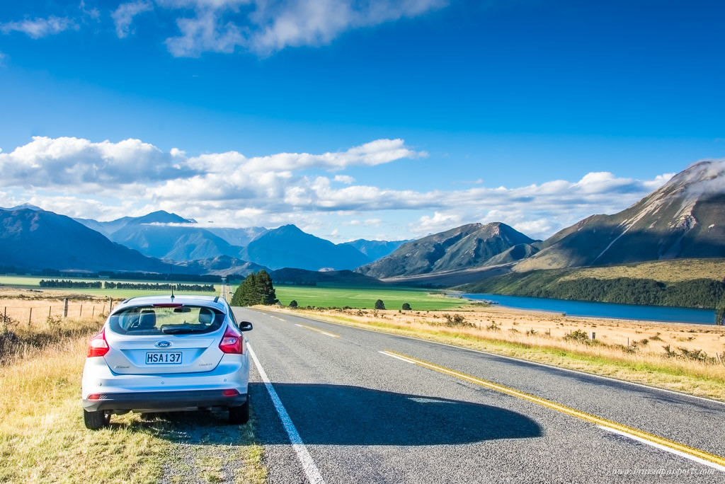 Silver car on a road in New Zealand, with blue sky and mountains in background